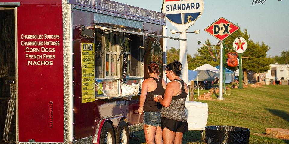 Guests ordering from a food vendor at TwisterFest beside vintage gas station signs